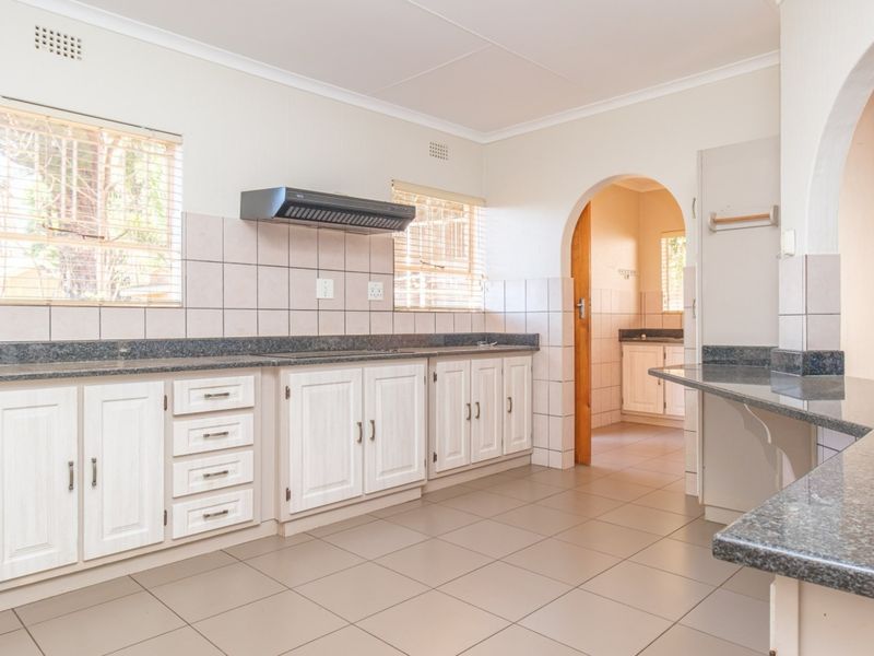 A spacious, empty kitchen featuring white built-in cabinetry, granite countertops, tiled backsplash, and an archway leading to an adjacent utility area.