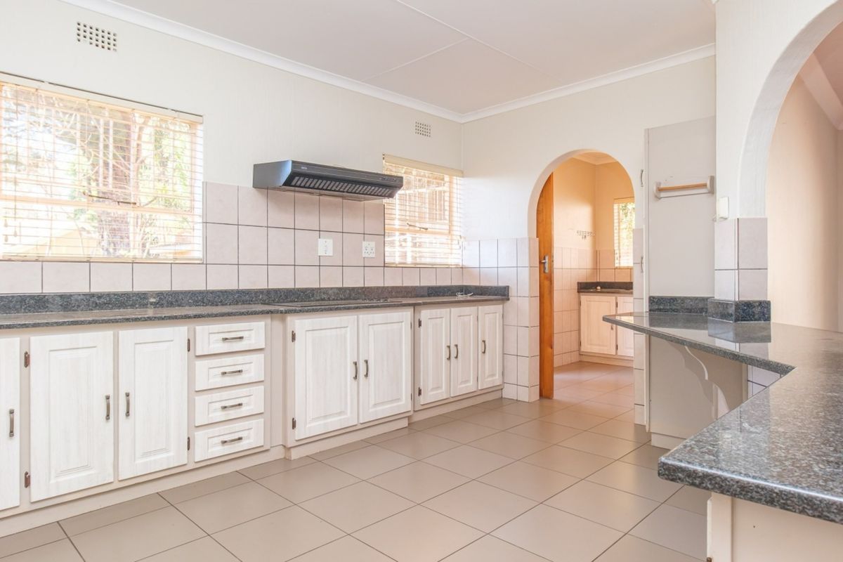 A spacious, empty kitchen featuring white built-in cabinetry, granite countertops, tiled backsplash, and an archway leading to an adjacent utility area.