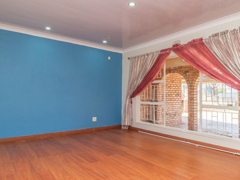 A bright, empty living room featuring laminate flooring, recessed downlighting, and a large window with views of an outdoor brick patio area.