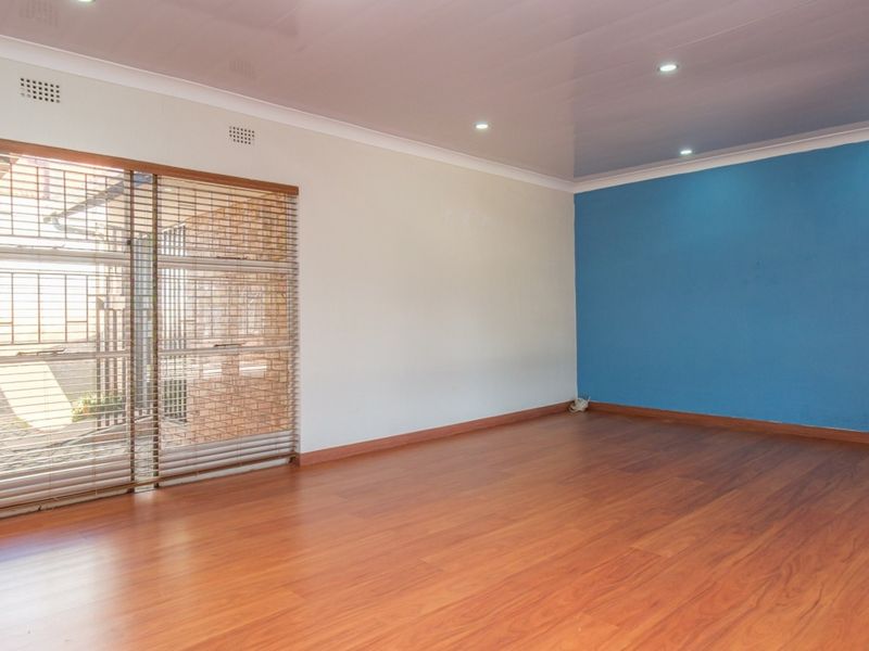Spacious living room featuring laminate flooring, recessed downlighting, and a sliding glass door with security gate and venetian blinds.