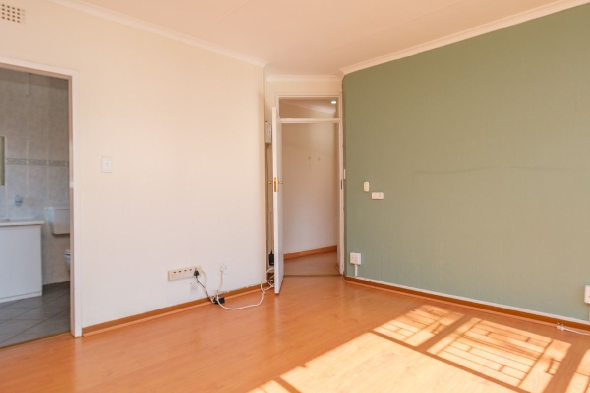 An empty bedroom featuring laminate flooring, a green accent wall, and direct access to an en-suite bathroom.