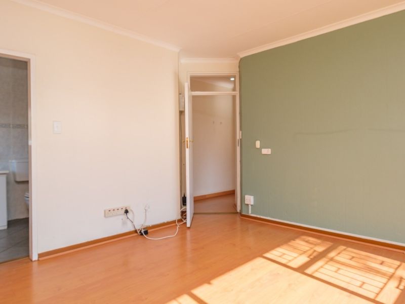 An empty bedroom featuring laminate flooring, a green accent wall, and direct access to an en-suite bathroom.