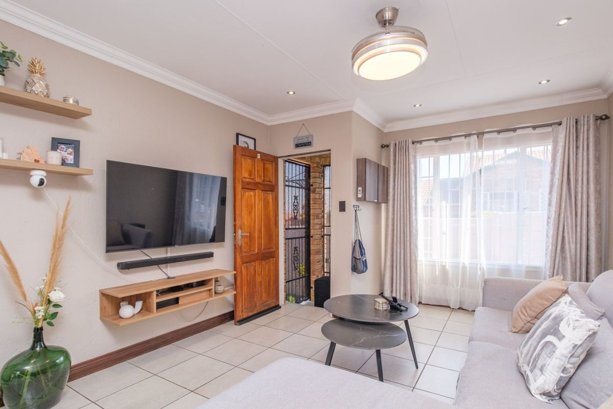 A well-maintained living room featuring tiled flooring, recessed lighting, a ceiling fan, and a timber entrance door with an integrated security gate.