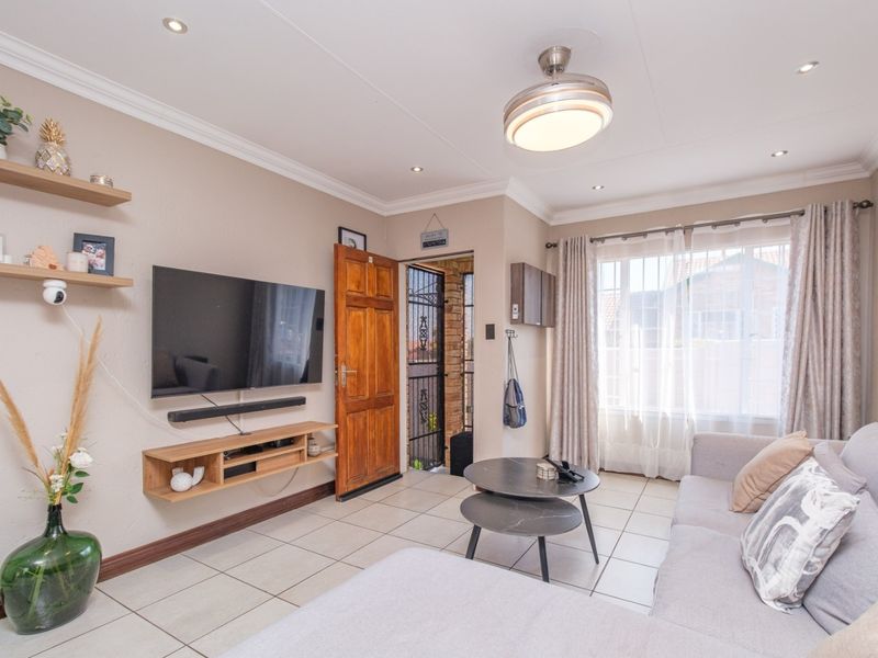 A well-maintained living room featuring tiled flooring, recessed lighting, a ceiling fan, and a timber entrance door with an integrated security gate.