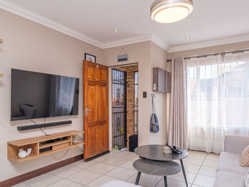 A well-maintained living room featuring tiled flooring, crown molding, recessed lighting, and direct access to the exterior through a timber door with security gate.