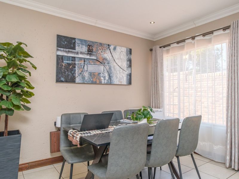 A well-lit dining area featuring neutral wall tones, tiled flooring, crown molding, and large windows with curtains, creating a comfortable and functional space.