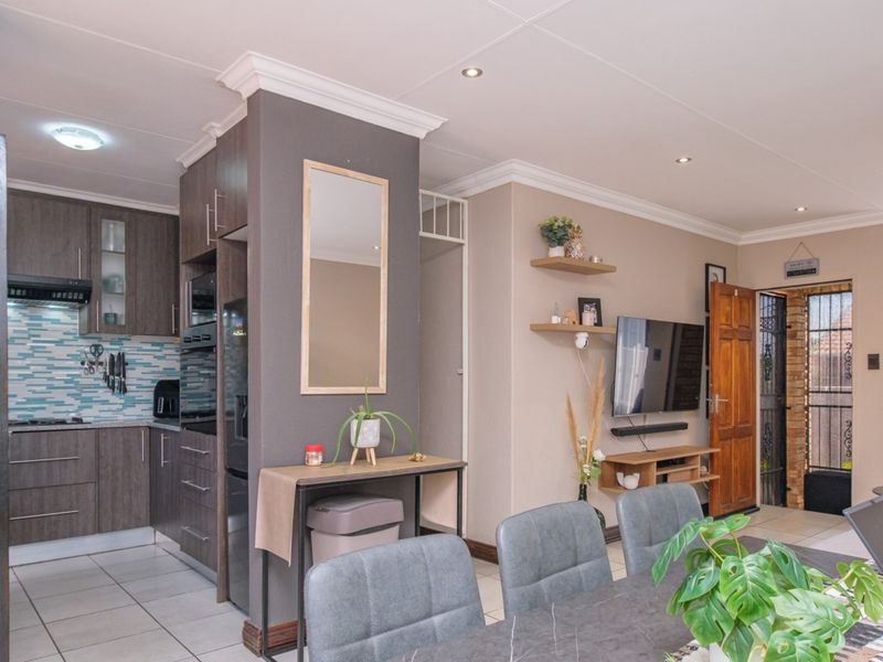 An open-plan living and kitchen area featuring modern dark cabinetry, a mosaic tile backsplash, tiled flooring, and recessed lighting, creating a functional and cohesive space.