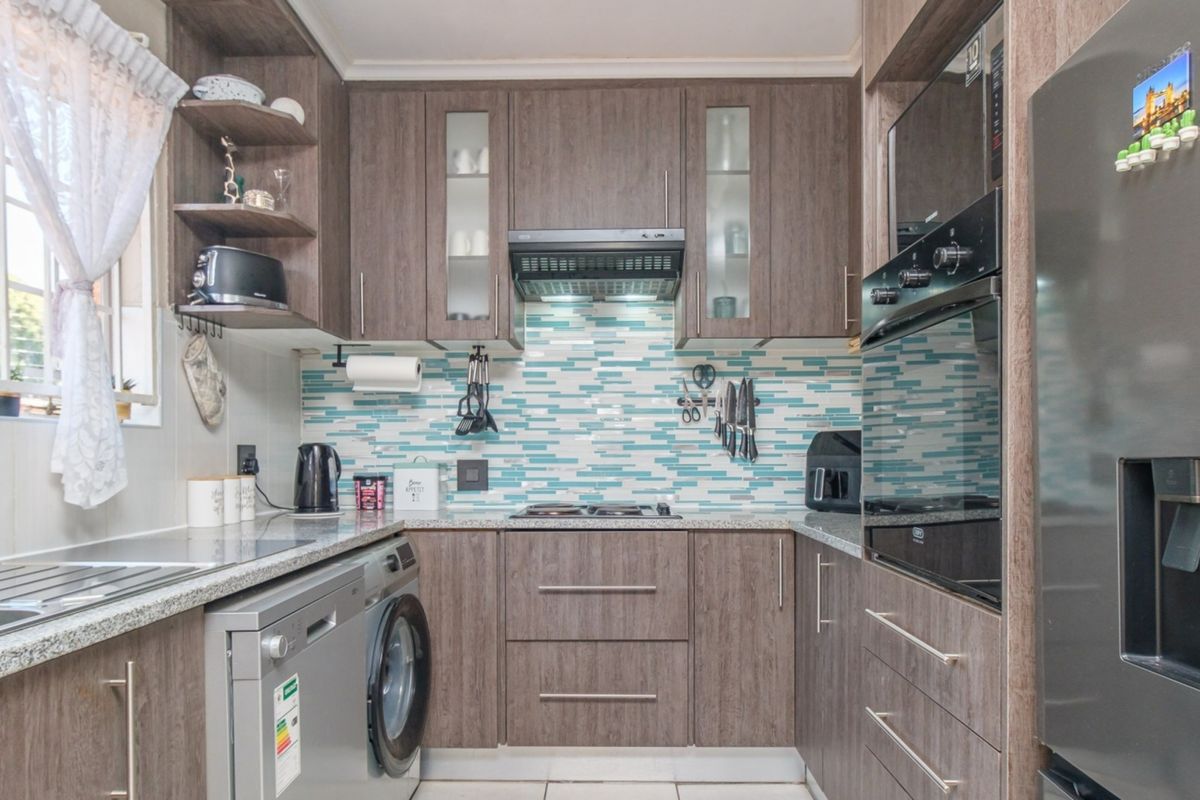 Modern kitchen featuring wood-look cabinetry, granite countertops, a vibrant mosaic backsplash, and integrated appliances including an oven and extractor fan.