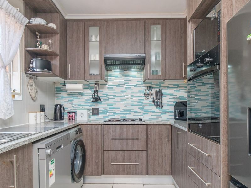 Modern kitchen featuring wood-look cabinetry, granite countertops, a vibrant mosaic backsplash, and integrated appliances including an oven and extractor fan.