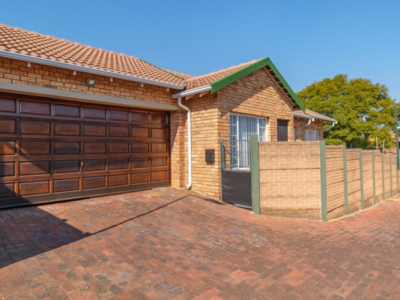 Front exterior view of a brick townhouse featuring a double garage, paved driveway, and secure gated entrance.