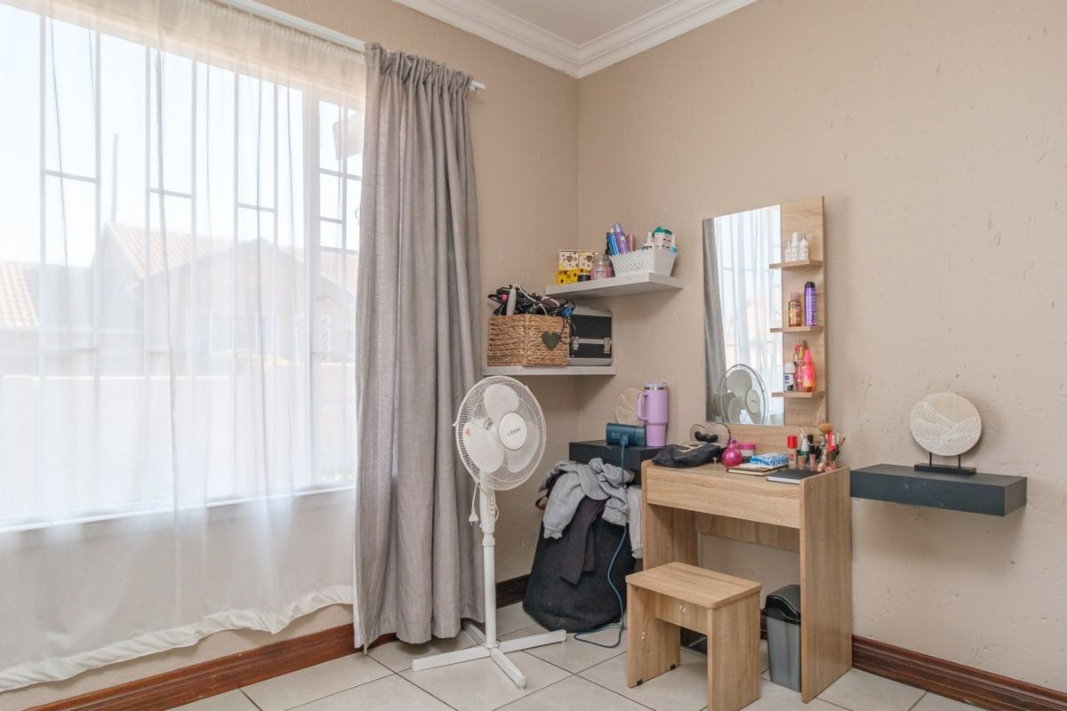 A bedroom featuring tiled flooring, neutral wall finishes, and a large window with security bars, providing natural light.