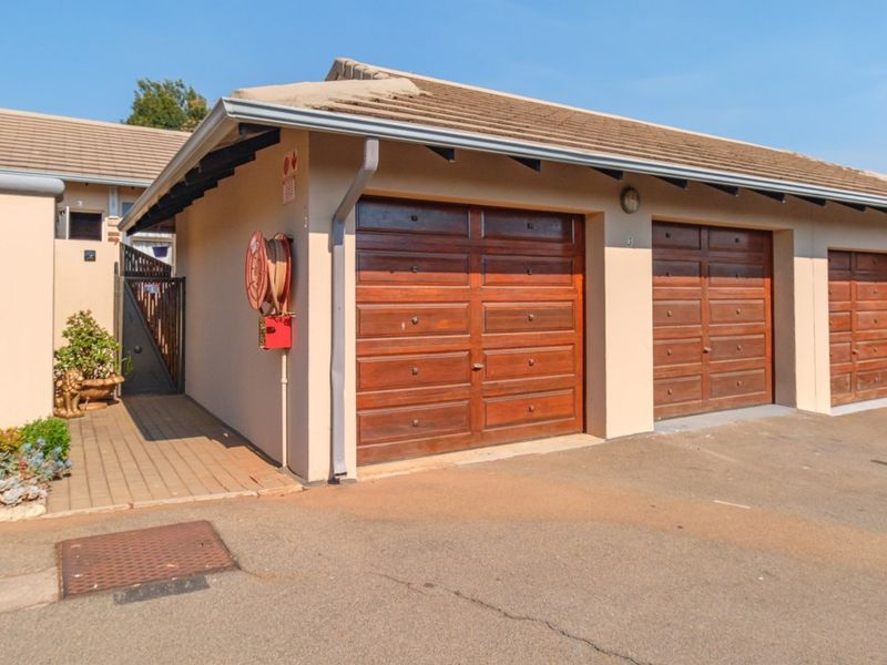 Exterior view of a townhouse complex featuring multiple wooden garage doors and a paved walkway with a fire hose reel.