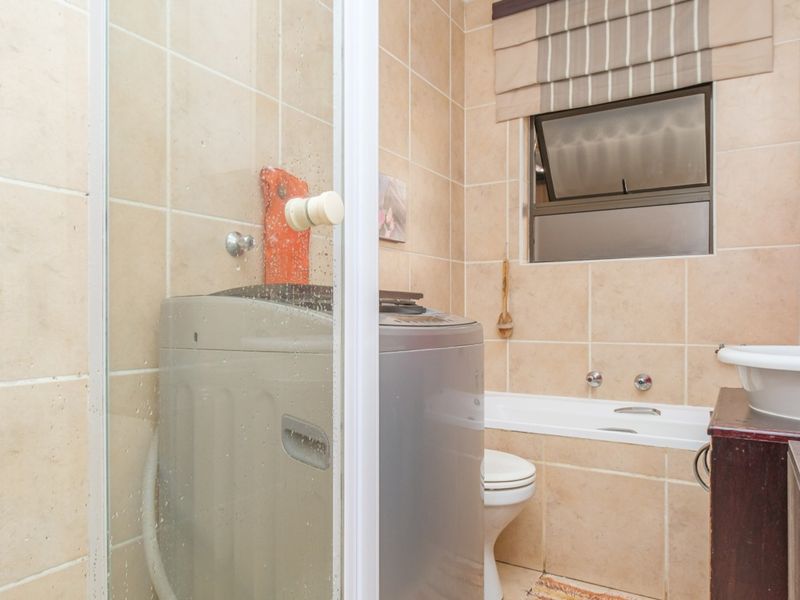 A functional bathroom featuring a shower enclosure, bathtub, toilet, and vanity basin, with integrated laundry facilities and neutral wall tiling.