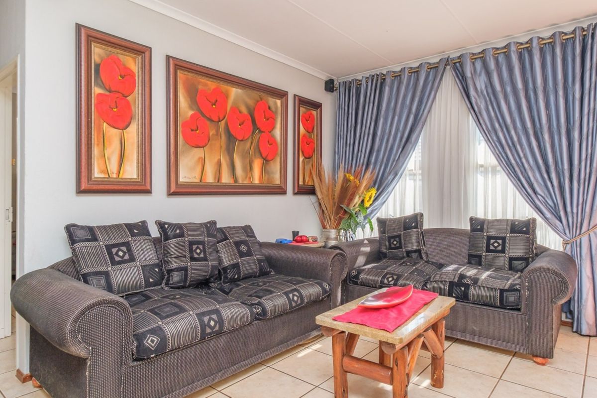 A comfortable living room featuring neutral tiled flooring and large windows dressed with curtains, providing a bright and functional space for relaxation.
