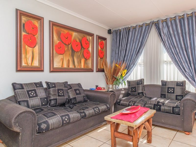 A comfortable living room featuring neutral tiled flooring and large windows dressed with curtains, providing a bright and functional space for relaxation.