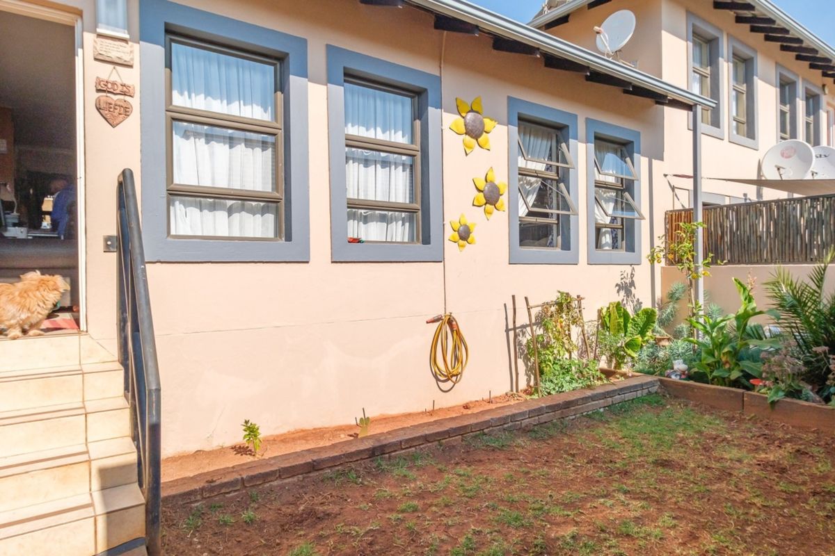Rear exterior view of the townhouse featuring a small garden area, tiled entrance steps with a metal handrail, and casement windows.