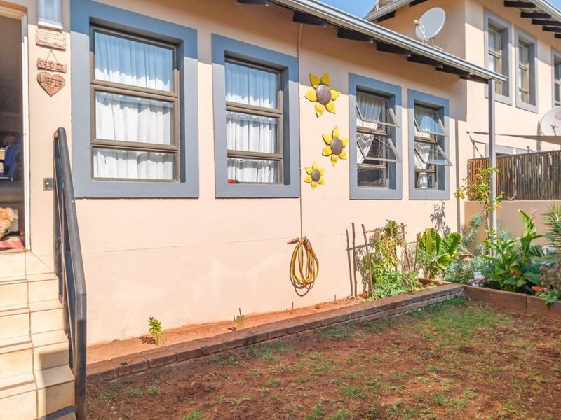 Rear exterior view of the townhouse featuring a small garden area, tiled entrance steps with a metal handrail, and casement windows.