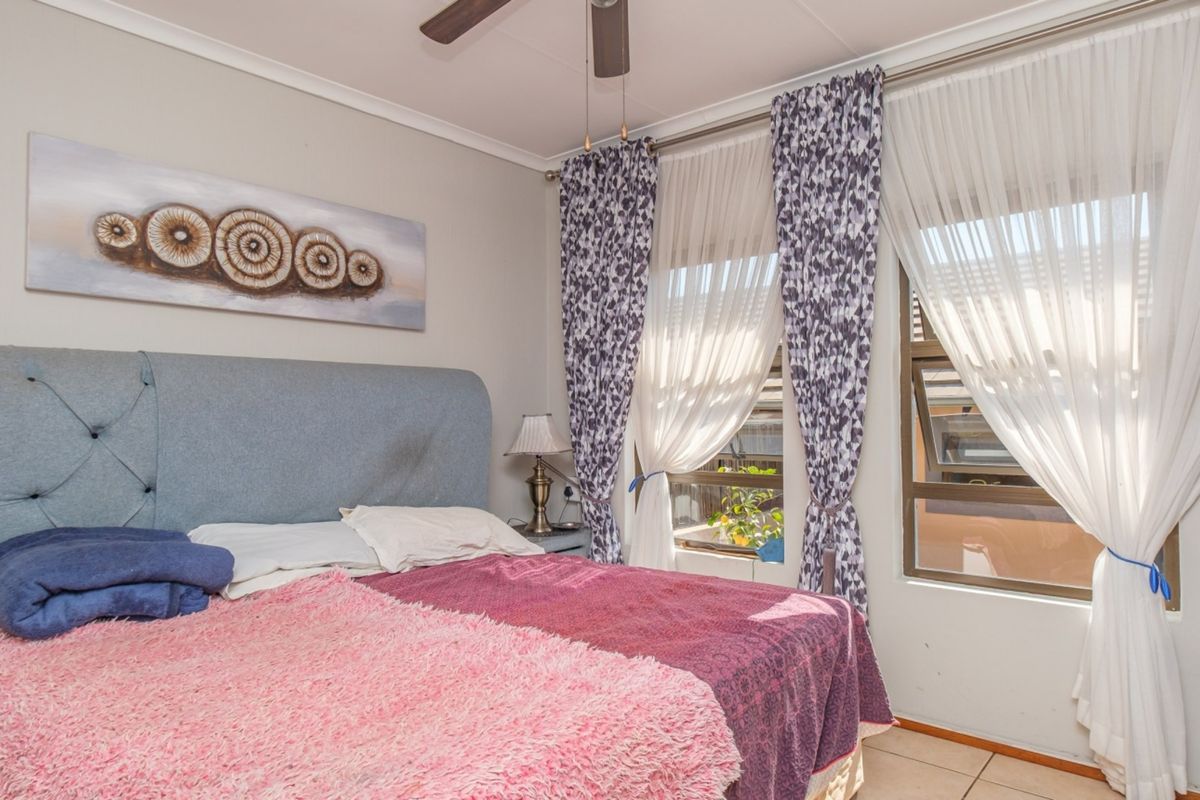 A well-lit bedroom featuring tiled flooring, a ceiling fan, and large windows that allow for ample natural light.