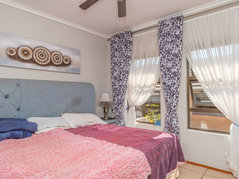 A well-lit bedroom featuring tiled flooring, a ceiling fan, and large windows that allow for ample natural light.