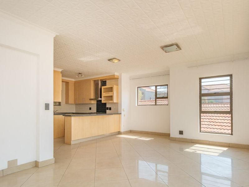 Spacious open-plan living area featuring tiled floors, a functional kitchen with built-in cabinetry, and large windows providing ample natural light.