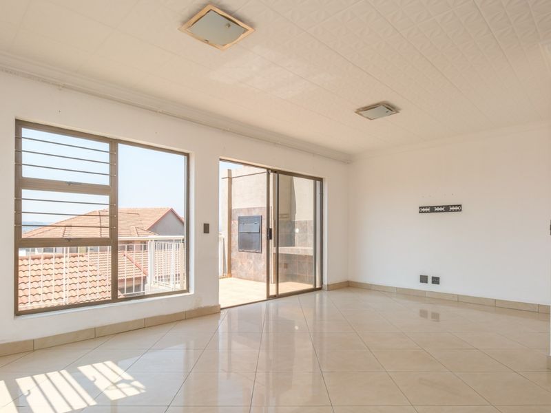 Spacious, light-filled living area featuring tiled flooring, large windows, and direct access to an outdoor patio through sliding glass doors.