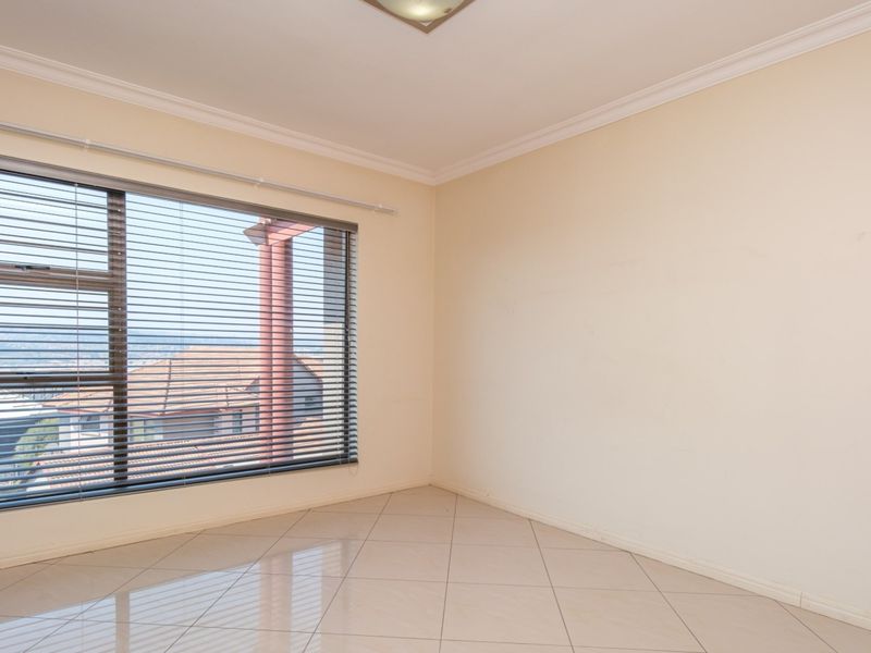 An empty bedroom featuring neutral tiled flooring, large aluminium-framed windows with venetian blinds, and classic ceiling cornicing.