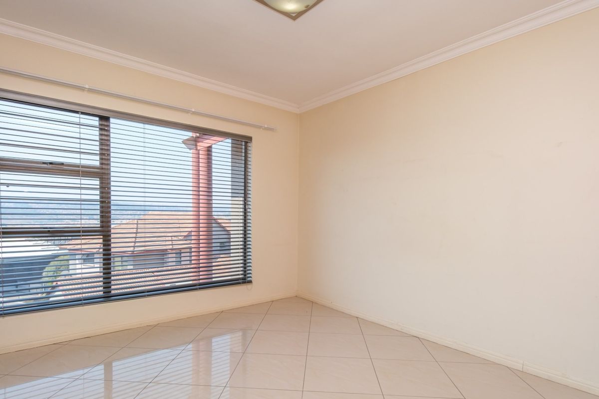 An empty bedroom featuring neutral tiled flooring, large aluminium-framed windows with venetian blinds, and classic ceiling cornicing.