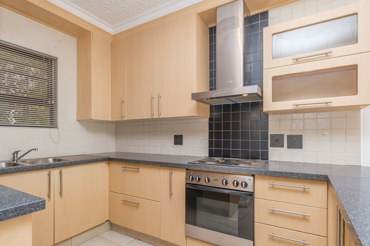 A functional kitchen featuring light wood cabinetry, granite countertops, a stainless steel oven with extractor fan, and a tiled backsplash.