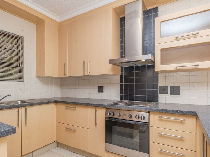 A functional kitchen featuring light wood cabinetry, granite countertops, a stainless steel oven with extractor fan, and a tiled backsplash.