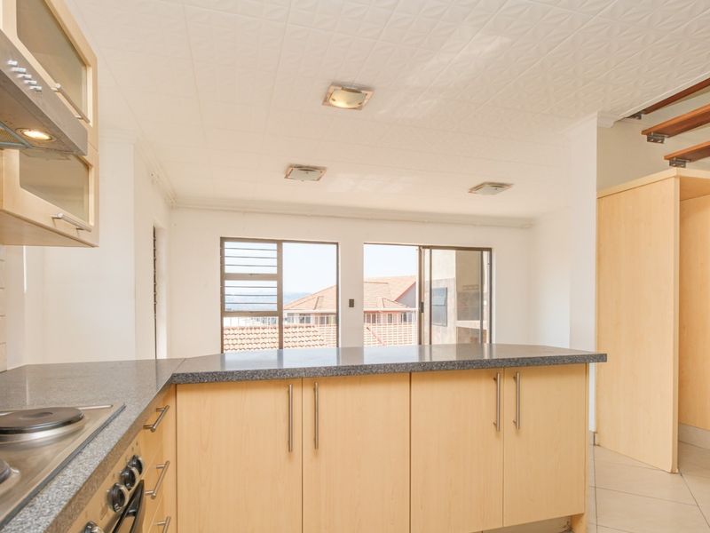A functional kitchen featuring light wood cabinetry, granite countertops, and an integrated hob and oven, with an open-plan layout and staircase access.