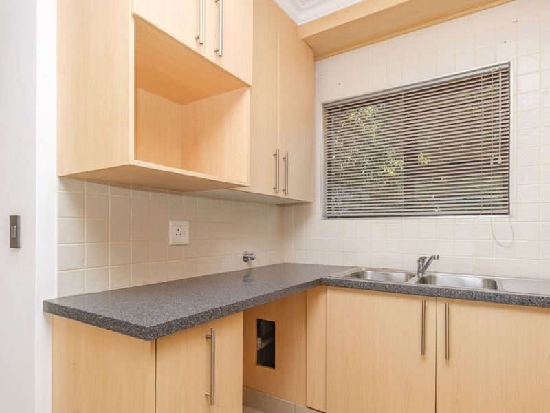 A functional kitchen featuring light wood-tone cabinetry, dark laminate countertops, a double stainless steel sink, and tiled splashbacks.