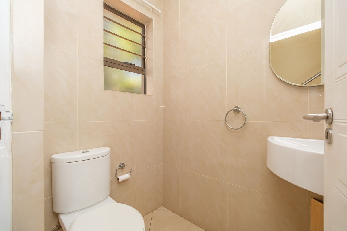 A compact, fully tiled bathroom featuring a modern toilet, wall-mounted basin, and a louvered window for ventilation.
