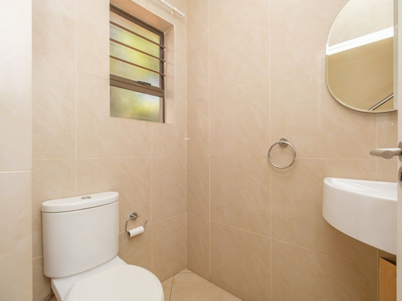 A compact, fully tiled bathroom featuring a modern toilet, wall-mounted basin, and a louvered window for ventilation.