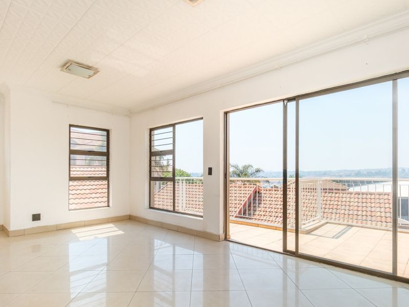 Bright and spacious open-plan living area featuring large windows, tiled floors, and sliding glass doors leading to a private balcony.