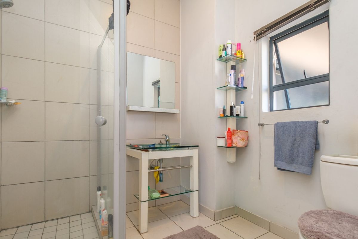 A functional bathroom featuring a glass shower enclosure, a modern glass vanity basin, and a standard toilet with tiled finishes throughout.