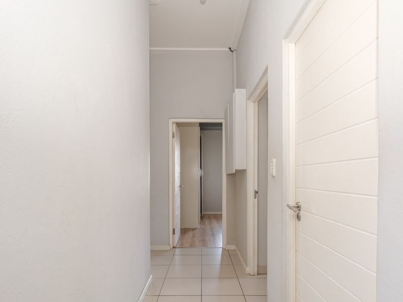 A clean, neutral-toned hallway featuring tiled flooring and multiple internal doors, providing access to various rooms within the apartment.