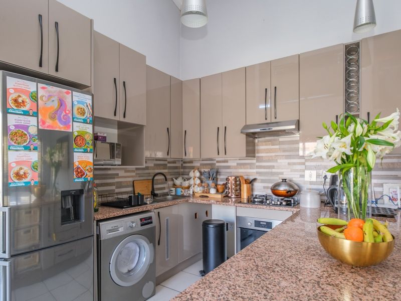 Modern kitchen featuring high-gloss cabinetry, granite countertops, a built-in oven with gas hob, and an integrated washing machine, offering a functional and contemporary workspace.