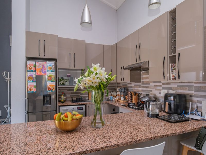 Modern kitchen featuring high-gloss cabinetry, granite countertops, a gas hob, and a tiled backsplash, offering a functional and contemporary cooking space.
