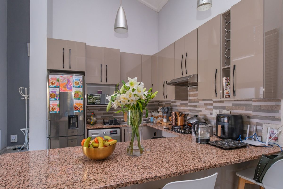 Modern kitchen featuring high-gloss cabinetry, granite countertops, a gas hob, and a tiled backsplash, offering a functional and contemporary cooking space.
