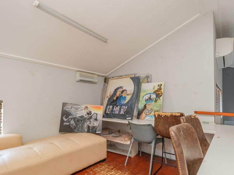A living area featuring timber flooring, a sloped ceiling, and a wall-mounted air conditioning unit, requiring cosmetic updates to improve its overall appeal.