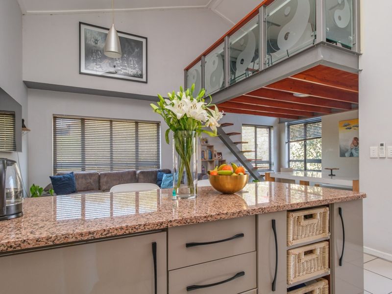 Open-plan living area featuring a modern kitchen with granite countertops, a mezzanine level with glass balustrades, and large windows providing natural light.