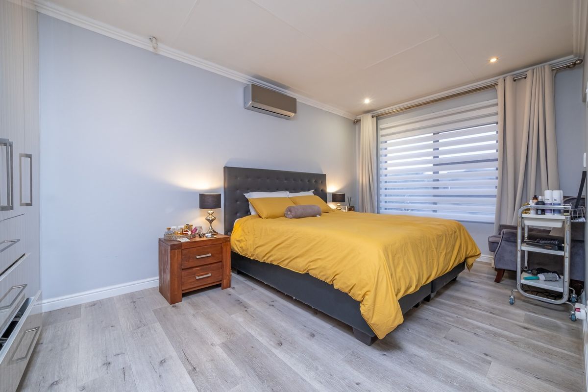 A well-maintained bedroom featuring modern laminate flooring, built-in cupboards, an air conditioning unit, and neutral wall finishes with recessed lighting.