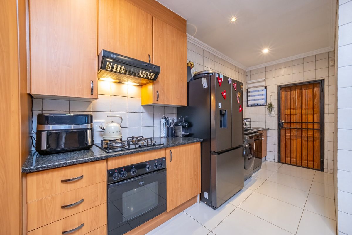 Functional kitchen featuring light wood cabinetry, granite countertops, gas hob, built-in oven, and tiled finishes with direct access to an exterior door.
