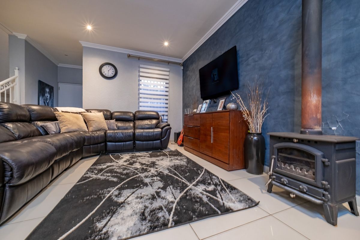 A comfortable living room featuring a dark textured accent wall, a freestanding fireplace, tiled flooring, and recessed lighting.