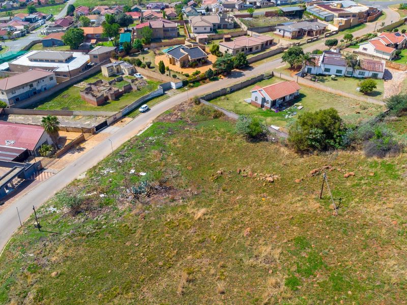 An aerial view of a vacant residential plot situated in a developed suburban neighborhood, showing surrounding street access and nearby residential properties.