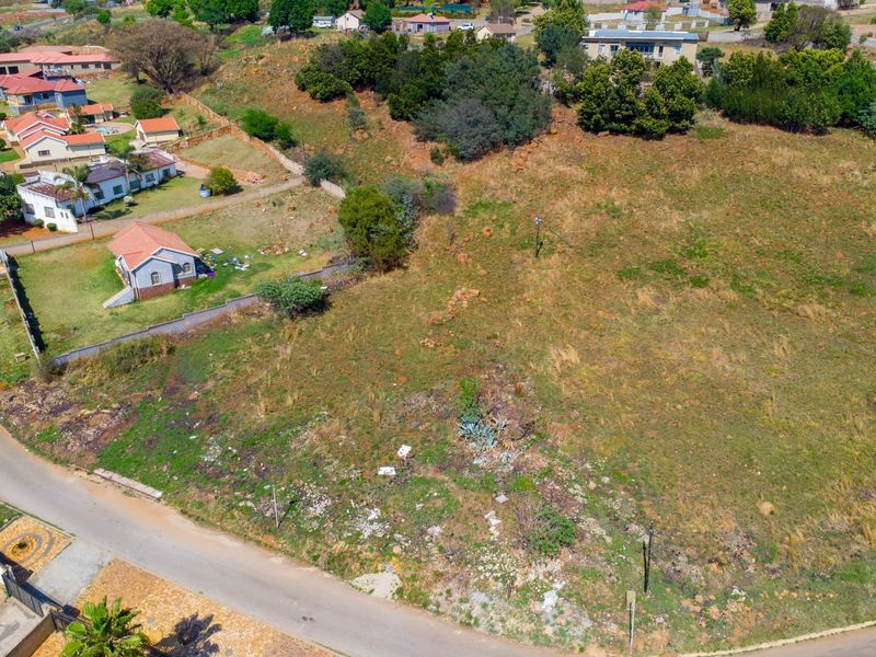 An aerial view of a vacant residential plot featuring natural vegetation, street access, and surrounding established residential properties.