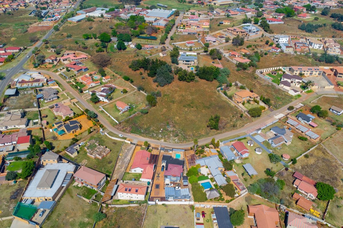 An aerial view of a residential neighborhood showcasing a vacant land plot surrounded by established housing and local infrastructure.