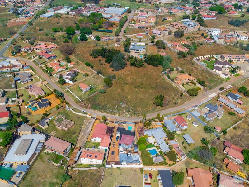 An aerial view of a residential neighborhood showcasing a vacant land plot surrounded by established housing and local infrastructure.