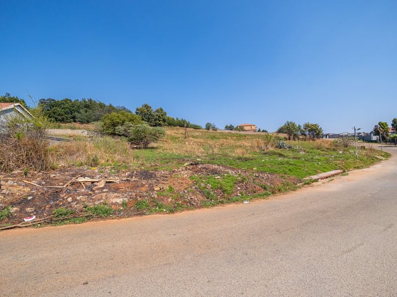 A vacant residential plot of land with street frontage, featuring natural vegetation and direct access to a paved road.