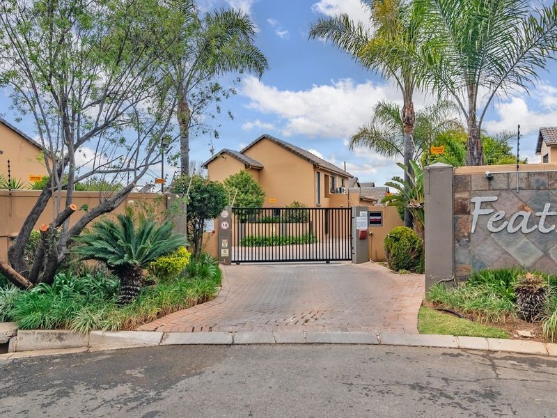 Entrance view of Feathers Hill complex featuring a secure gated access point, paved driveway, and perimeter wall with electric fencing.